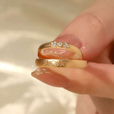 Close-up of two solid gold rings—trio-diamond band stacked on matte sunburst band between fingers